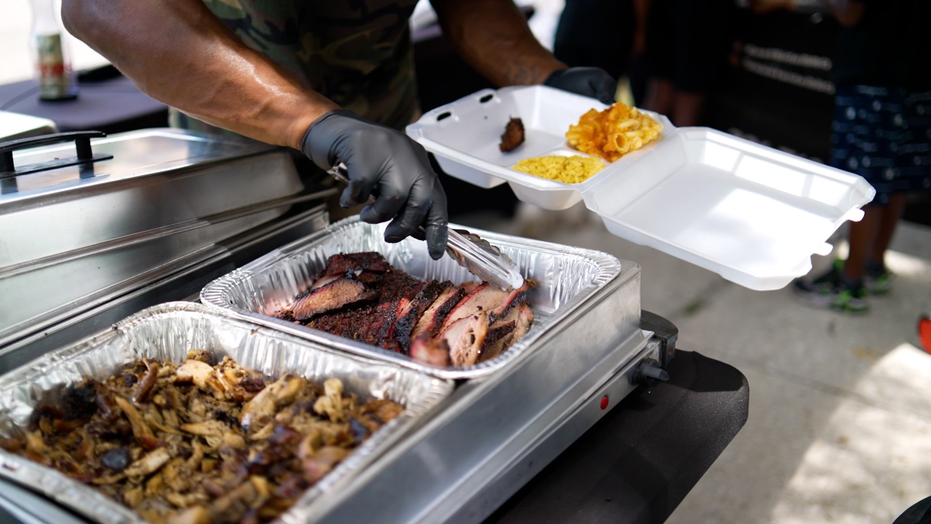 Sliced smoked meat and sides being served into a guest’s plate