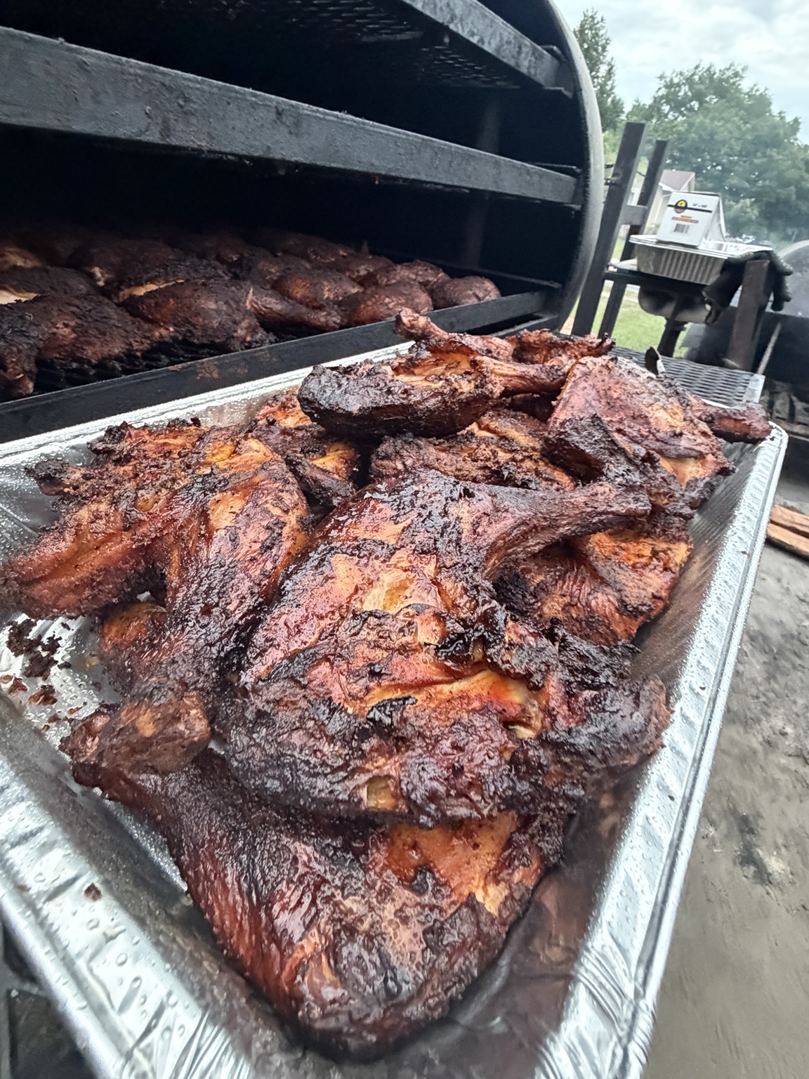 Eastside BBQ smoked chicken leg quarters piled in a tray beside the smoker